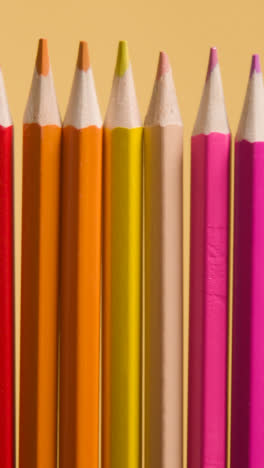 Vertical-Video-Studio-Shot-Of-Multi-Coloured-Pencils-In-A-Line-On-Yellow-Background-1